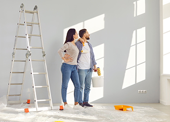 Happy married couple painting wall in their new house with paint rollers get_loan_against_your_property_or_refinance
